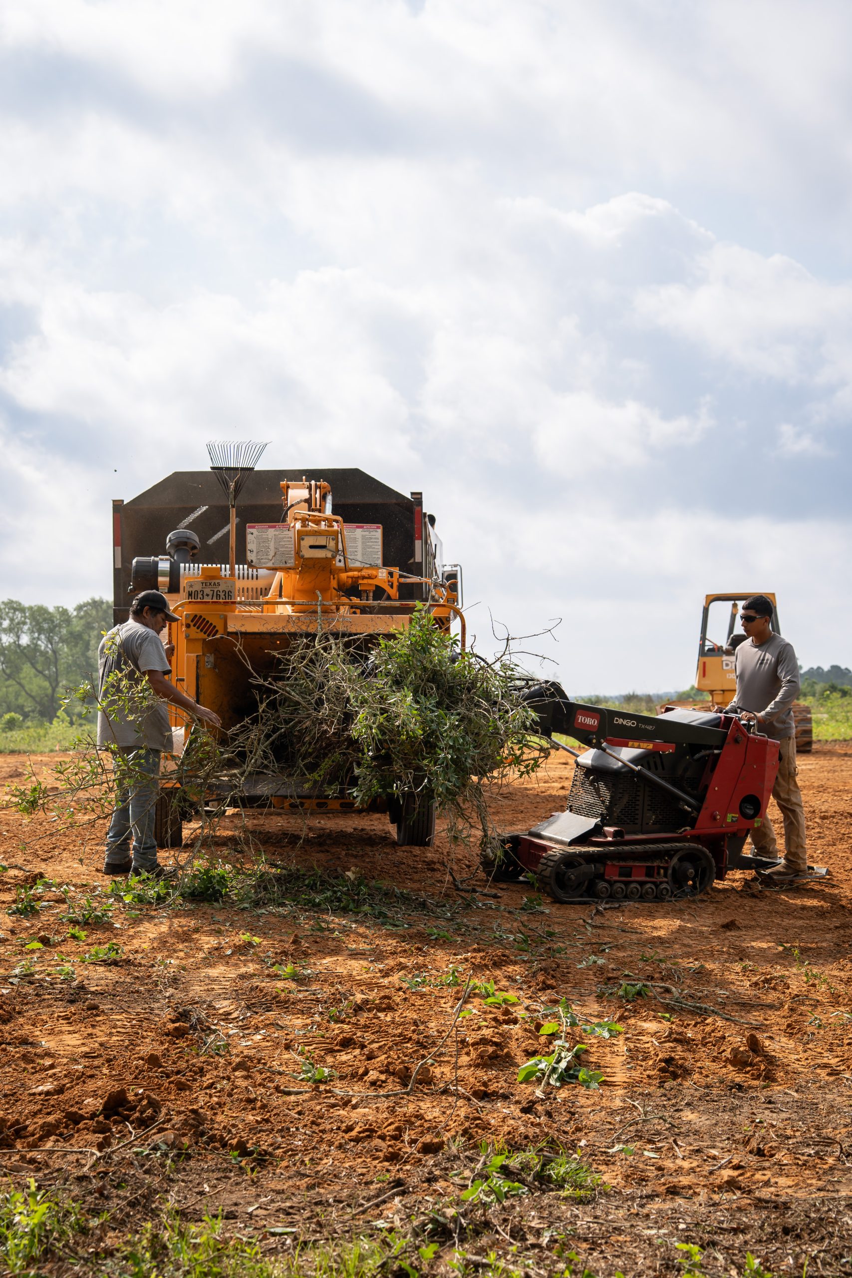 A stump grinder machine clears a tree stump in a wooded outdoor work site.